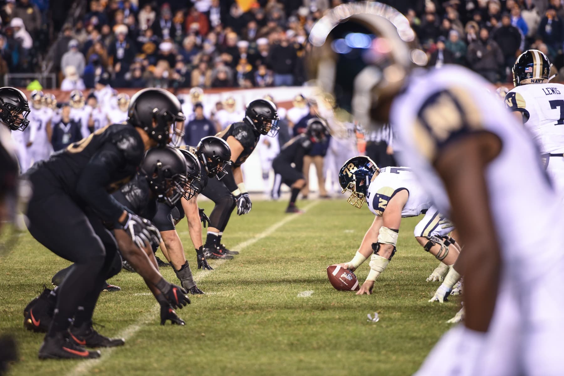 Las líneas de Army, de negro, y de Navy, de blanco, frente a frente en la línea de scrimmage durante el Army–Navy Game de 2018 en Filadelfia, con el estadio lleno al fondo.